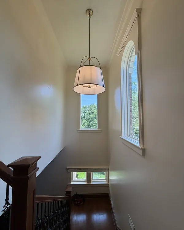 Drum pendant light installed beside an arched stairwell window